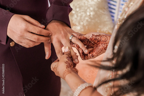 Tender hands on an Indian Bride covered with henna art holding Groom's hand while she give him an Engagement Ring 