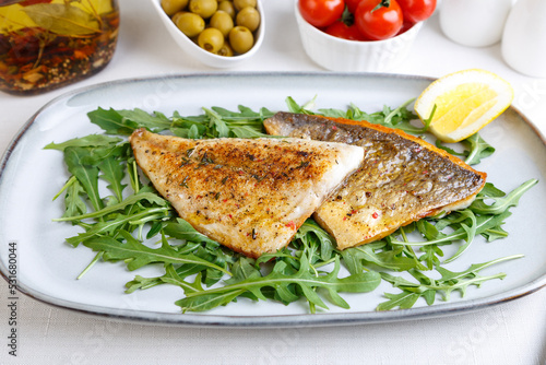 Fried dorado fillet with crispy skin. Arugula, cherry tomatoes, olives, lemon and olive oil. Traditional Mediterranean dish. White background. Selective focus, close-up.