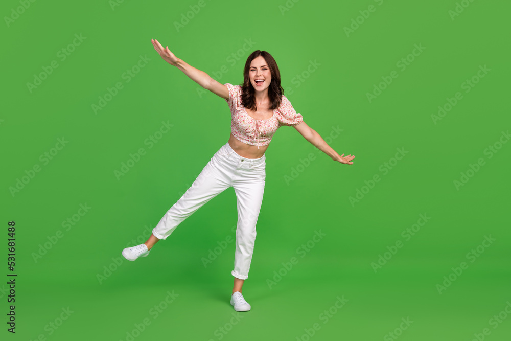 Full length photo of cute gorgeous girl with curly hairstyle dressed white trousers top hold balance isolated on green color background