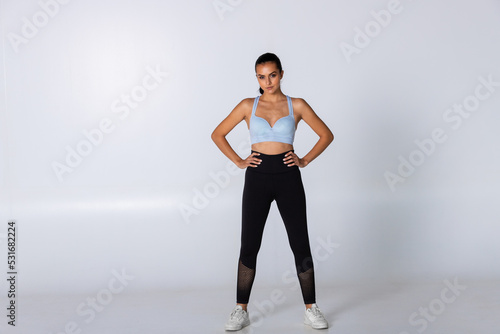Female trainer standing strong with hands on hips on white background, woman at gym standing before exercise looking at camera