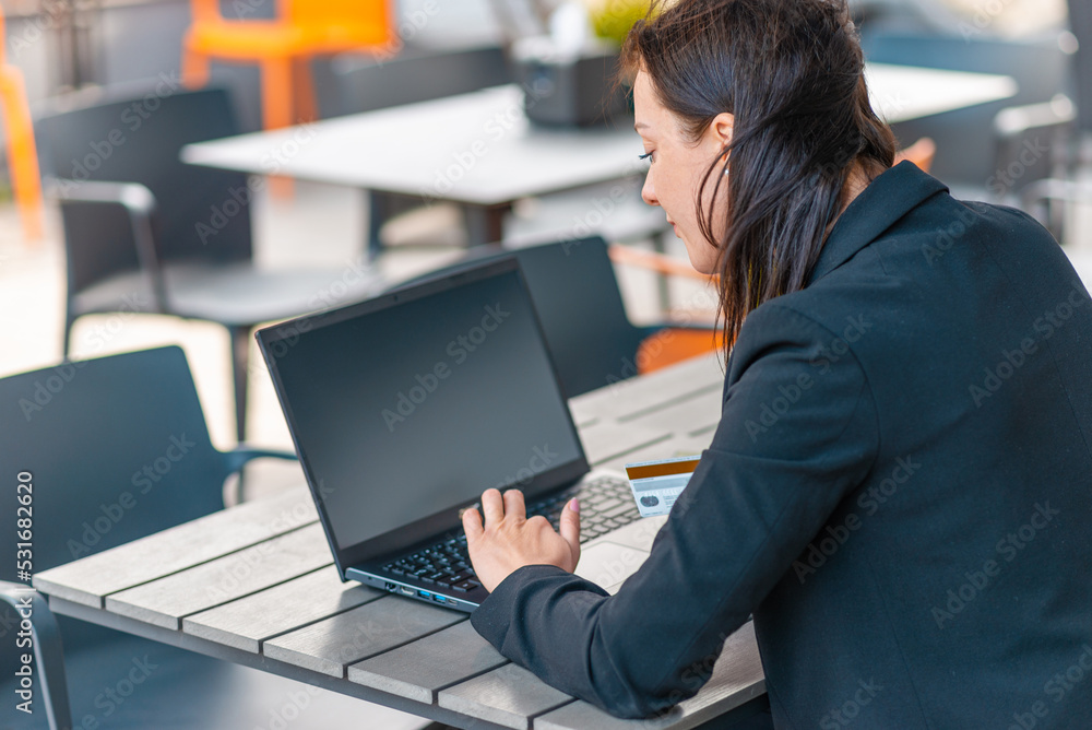 Young brunette business woman dressed in black suit spending her lunch time at street cafe terrace,drinking coffee.buy by credit card on her laptop.Closeup. Young brunette business woman dressed in black suit spending her lunch time at street cafe terrace,drinking coffee.buy by credit card on her laptop.Closeup.