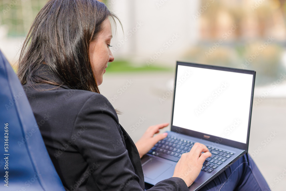 Blank white screen.Mockup.Young brunette business woman use laptop computer outdoor cafe.She dressed in black suit spending her lunch time at street cafe terrace.Close-up.Selective focus. Blank white screen.Mockup.Young brunette business woman use laptop computer outdoor cafe.She dressed in black suit spending her lunch time at street cafe terrace.Close-up.Selective focus.