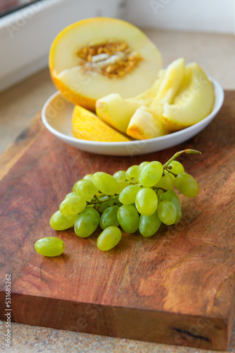 a plate of melon slices, green grapes on a wooden background, kitchen windowsill, concept of fresh fruits and healthy food