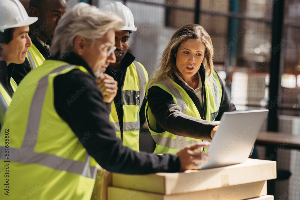 Warehouse employees having a discussion using a laptop Warehouse employees having a discussion using a laptop