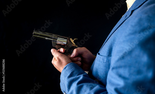 Sniper man in black suit gesturing and boldly holding gun on isolated black background. © RomanR