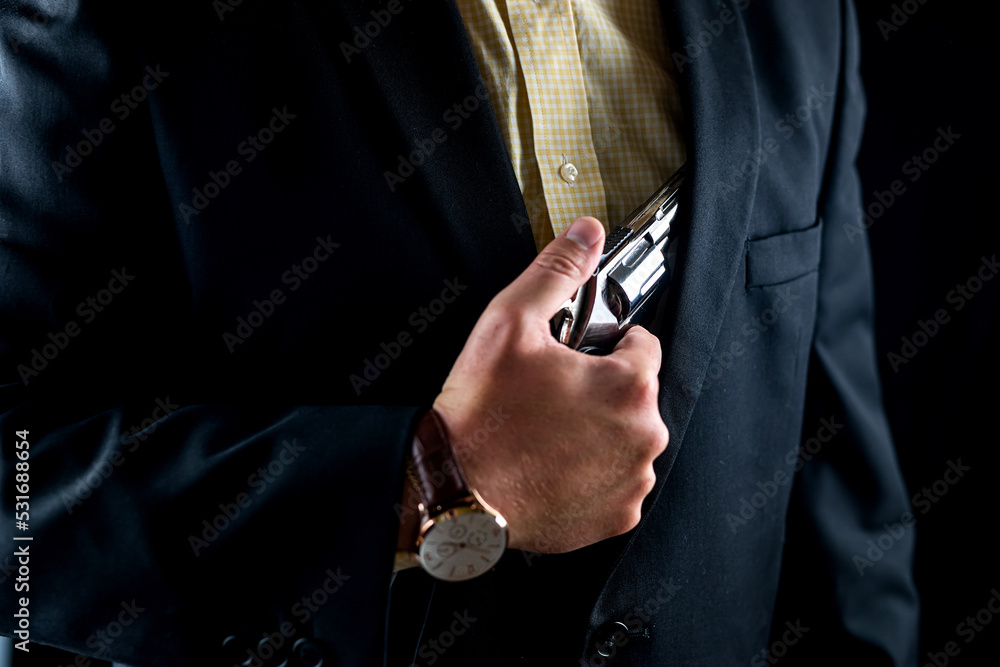one male spy in a professional tuxedo holds a revolver pistol before the start of a film shoot.
