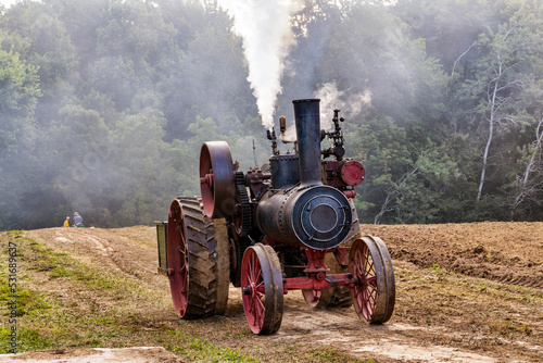 Old steam engine moving through rural farm field. photo