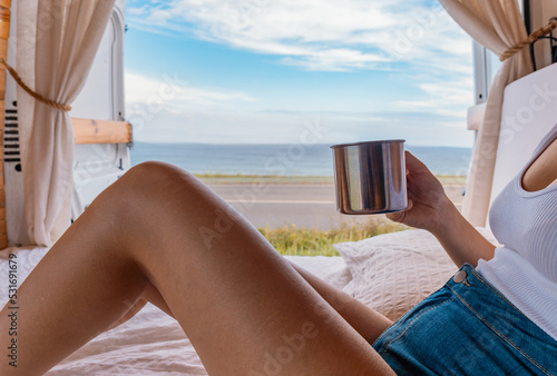 Cuadro en lienzo Detalle de mujer irreconocible con la taza en la mano, acostada en la cama de la camper, con vistas al mar
