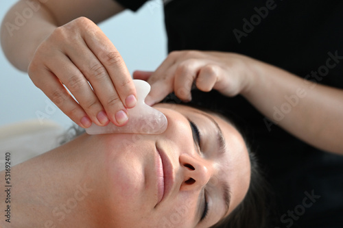 Cosmetologist does a facial massage with a gouache scraper. close up. Professional anti-aging facial massage.