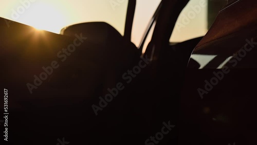 Young attractive girl in light clothes opens the door of red car and gets out of it in parking lot at sunset. Cinematic slow motion footage with rays of the setting sun. Girl driver, lifestyle, travel