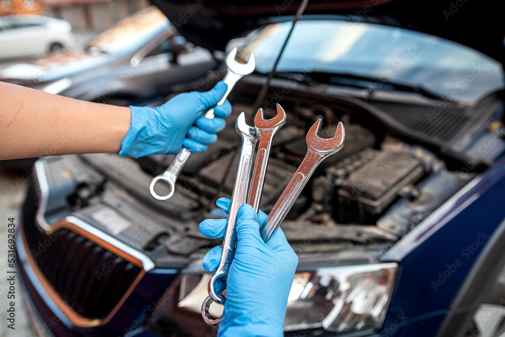 Close-up of auto mechanic's hands using wrench to repair car engine in auto garage.