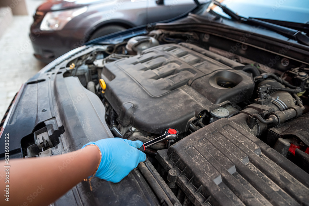 car mechanic repairs a car engine near a car with an open hood. car mechanic repairs a car engine near a car with an open hood.