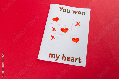 Paper with you won my heart inscription. Tic tac toe. Romantic love declaration on red background. photo