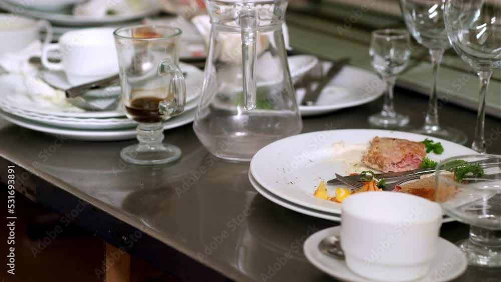 Dirty cups and plates with leftovers and silverware placed on metal table ready for dish washing in restaurant kitchen Dirty cups and plates with leftovers and silverware placed on metal table ready for dish washing in restaurant kitchen
