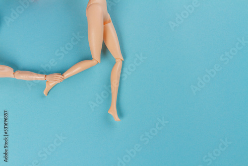 Top view doll hand touching womans leg. Blue background with copy space.