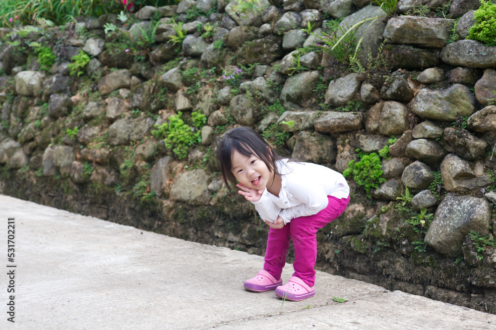 An Asian kid in a white shirt and purple pants in action with a smiley face in natural daylight. An Asian girl kid with rocks in the background. An Asian kid in a white shirt and purple pants in action with a smiley face in natural daylight. An Asian girl kid with rocks in the background.