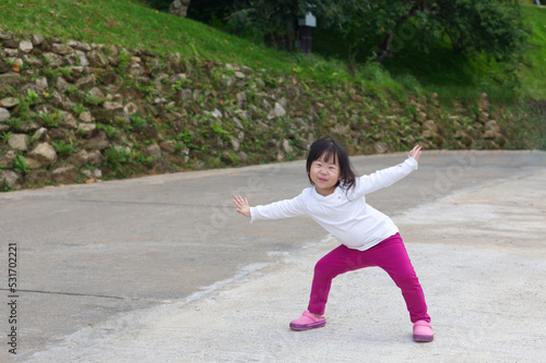 An Asian kid in a white shirt and purple pants in action with a smiley face in natural daylight. An Asian girl kid with rocks in the background.