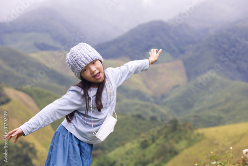 An Asian kid in a white shirt and purple pants in action with a smiley face in natural daylight. An Asian girl kid with rocks in the background.