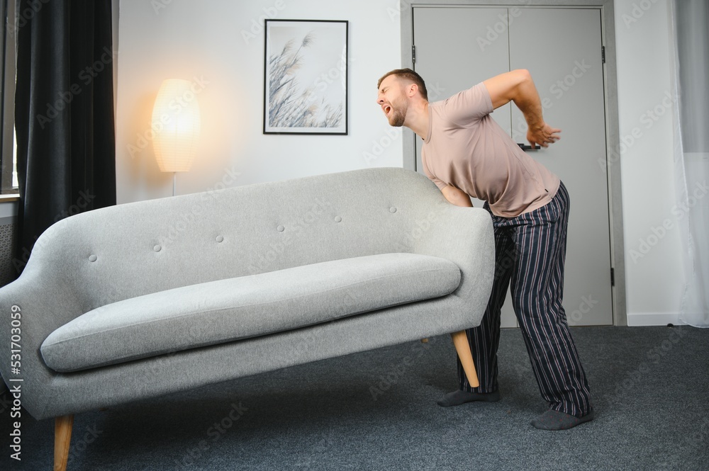 Obraz premium Young man suffering from back pain after carrying heavy furniture.