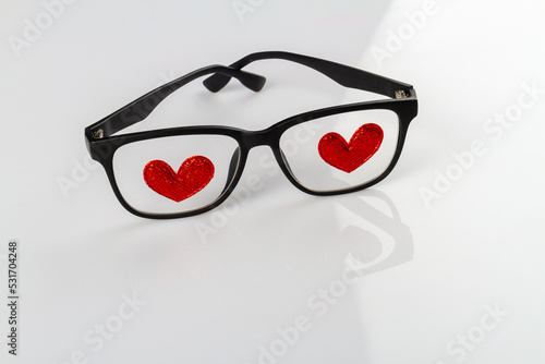 Close up glasses with red hearts atteched to lenses. White reflective background. photo