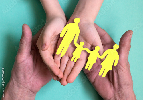 Tableau sur toile the hands of a man and a child hold a silhouette of a family with children cut out of yellow paper