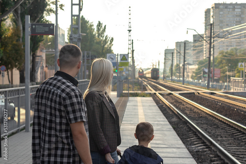 a family of three waiting on an empty railway platform for the arrival of a train