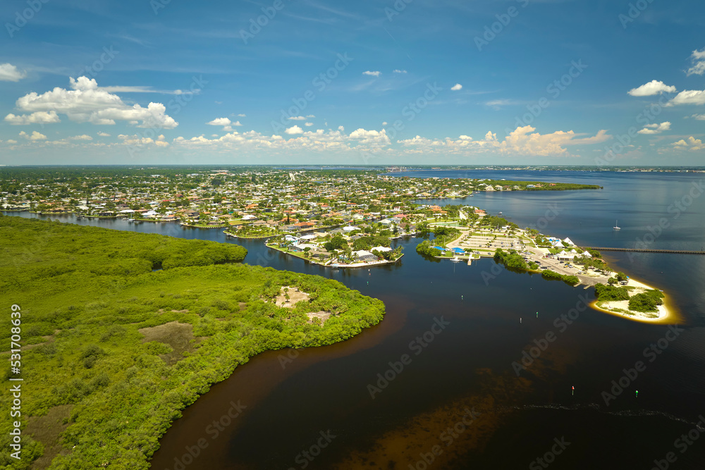 Aerial view of rural private houses in remote suburbs located near Florida wildlife wetlands with green vegetation on sea bay shore. Living close to nature concept