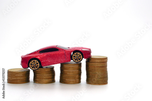 Small red car model on a large amount of stacked coins. Economy and business concept.