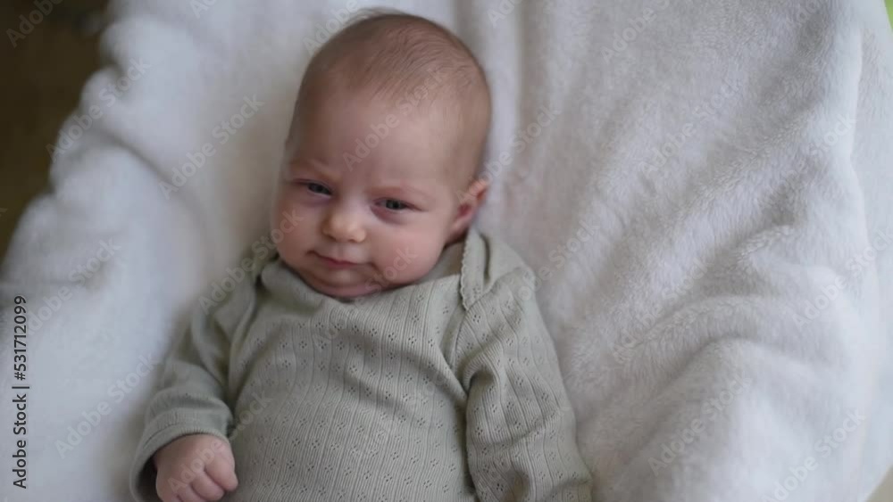 Newborn in olive overall lies in child seat on white blanket. Kid with surprise face. Childs - happiness for family. New worries and lifestyle. close up Newborn in olive overall lies in child seat on white blanket. Kid with surprise face. Childs - happiness for family. New worries and lifestyle. close up