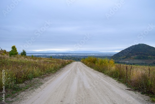 Gravel road leading down from the mountain on the background of the mountain, forest and fog