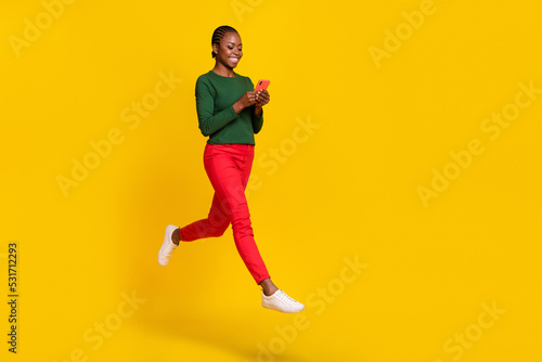 Full length photo of sweet pretty lady dressed green shirt jumping high chatting gadget empty space isolated yellow color background