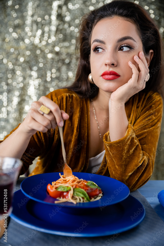 young woman in velour dress looking away near blue plate with spaghetti on glitter background. young woman in velour dress looking away near blue plate with spaghetti on glitter background.