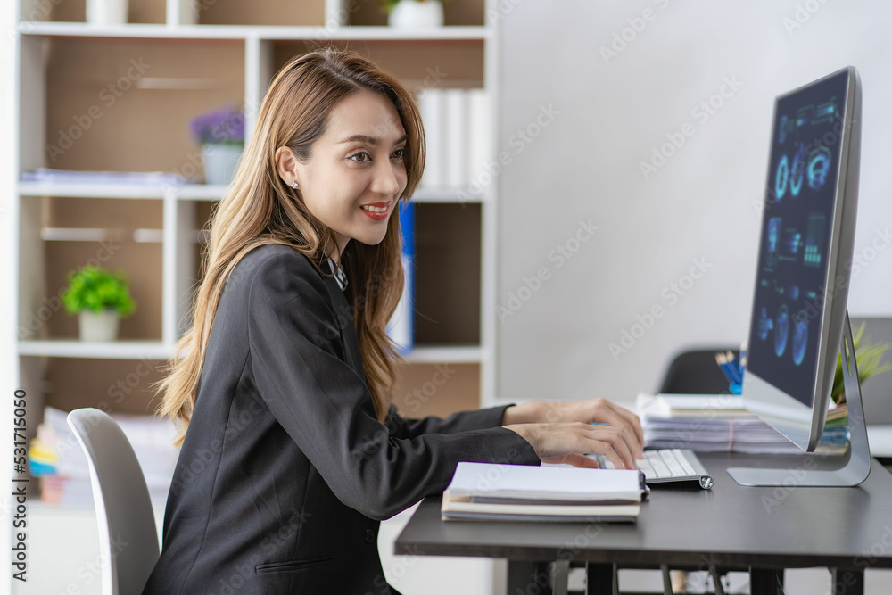 Smiling businesswoman working in office with money chart document and holding pen using laptop sitting on chair at studio in office accounting concept Smiling businesswoman working in office with money chart document and holding pen using laptop sitting on chair at studio in office accounting concept