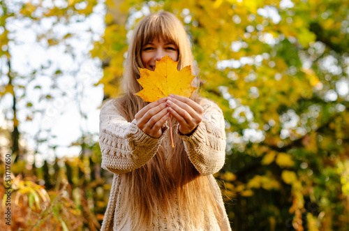 Beautiful autumn woman standing near colorful autumn leaves. Pretty happy cheerful model looking at camera. Young woman with autumn leaf in hand  autumn mood  relaxation  walking in nature