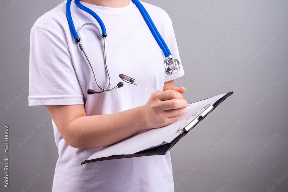 A medical worker without a face with a stethoscope on his neck writes a diagnosis on a gray background A medical worker without a face with a stethoscope on his neck writes a diagnosis on a gray background