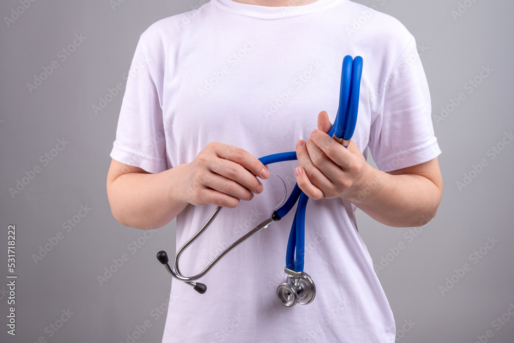 A medical worker without a face holds a stethoscope in his hands on a gray background