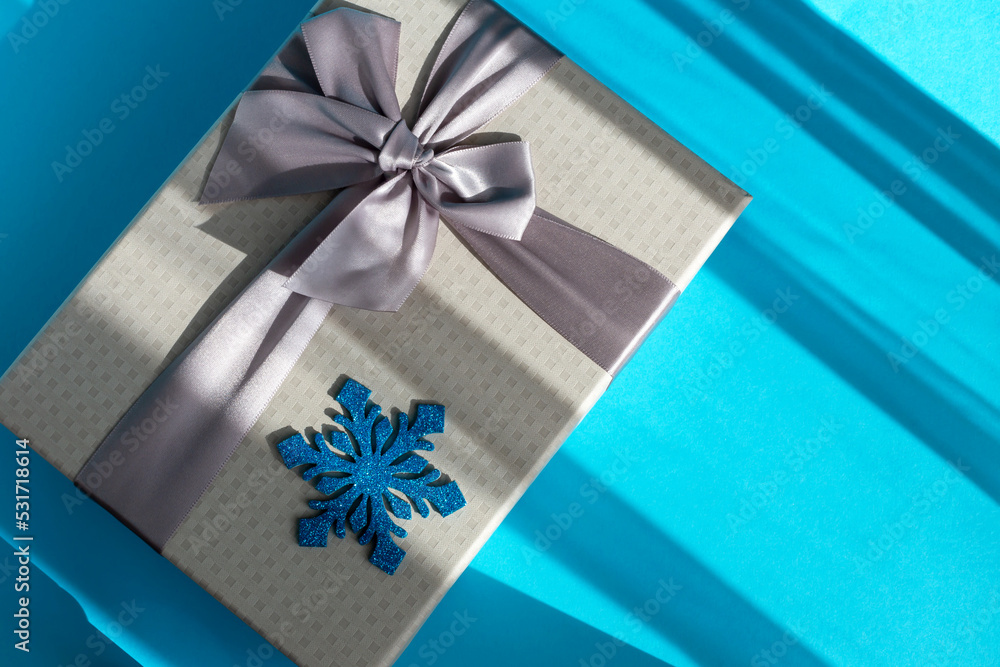Fototapeta premium Gray gift box with bow and snowflake on blue background