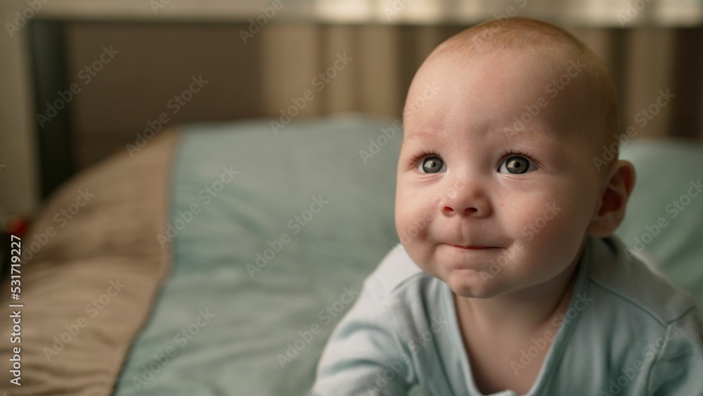 Half year old baby in striped casual clothes. Advertisement for children's products. A little boy in a white shirt sits and crawls on the bed. The little boy is sitting on the bed. Half year old baby in striped casual clothes. Advertisement for children's products. A little boy in a white shirt sits and crawls on the bed. The little boy is sitting on the bed.