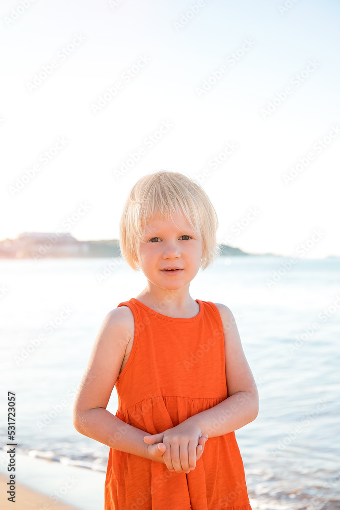 A pretty girl with blonde hair in an orange dress is enjoying her summer vacation, posing on a beautiful beach. A pretty girl with blonde hair in an orange dress is enjoying her summer vacation, posing on a beautiful beach.
