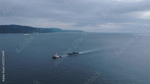 Flying toward small tug boat pulling barge through coastal waters at dusk