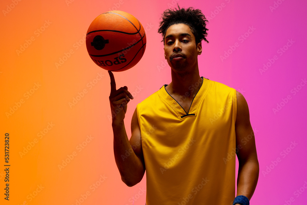 Image of biracial basketball player spinning basketball on pink to orange background Image of biracial basketball player spinning basketball on pink to orange background