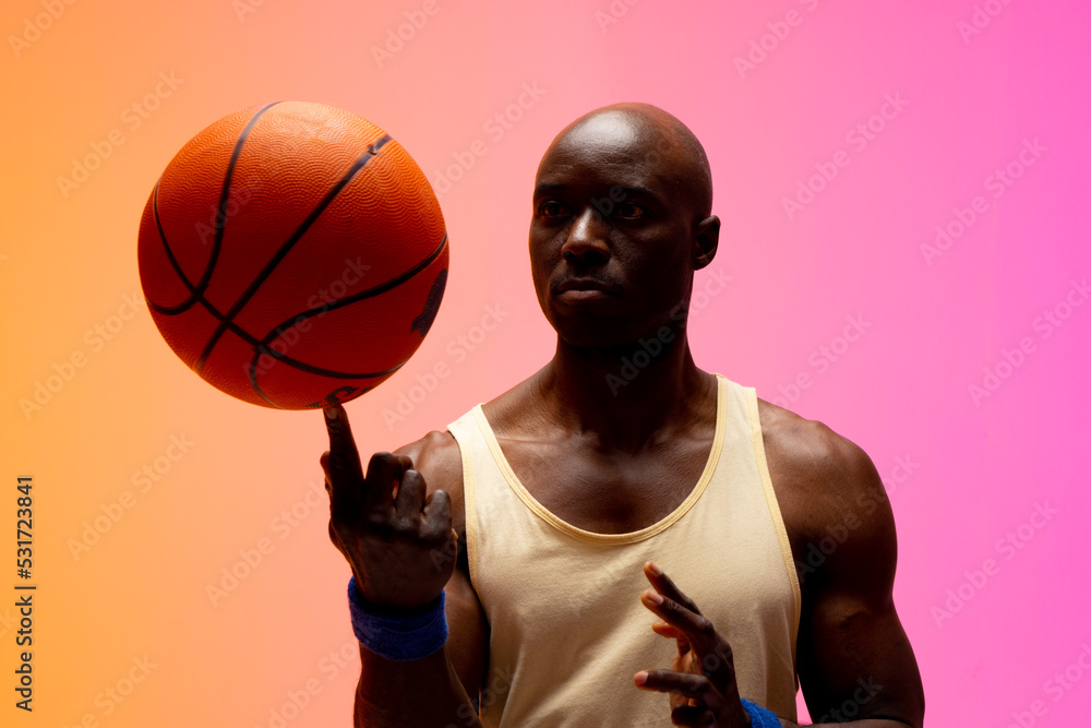 Image of african american basketball player playing with basketball on orange to pink background