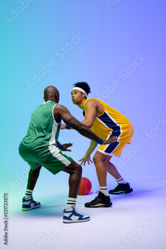 Image of two diverse basketball players with basketball playing on purple to green background