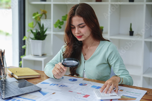 accountant holding a magnifying glass and using a calculator to check financial statements