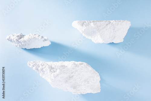 Styrofoam podiums for presentation cosmetic products or goods as elegant white islands fly in abstract blue sky in hard light with shadows in elegant grunge modern style. Template stage for design.