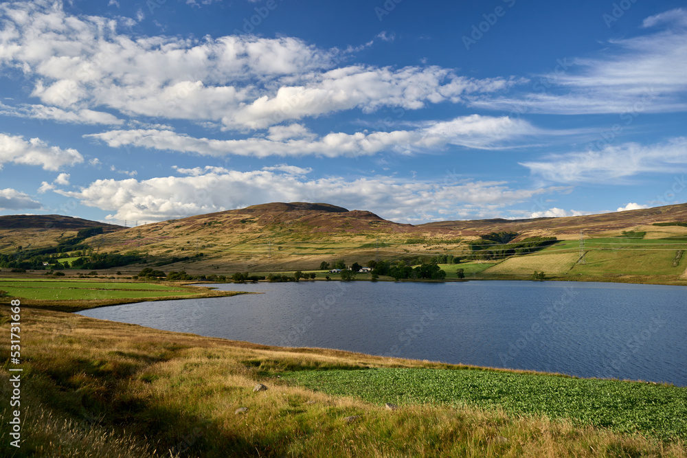 Scotland's Glen Quaich has a lake, lush farmland, and a woodland beneath a brilliant sky.