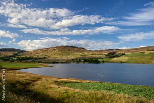 Scotland's Glen Quaich has a lake, lush farmland, and a woodland beneath a brilliant sky. © Valentine