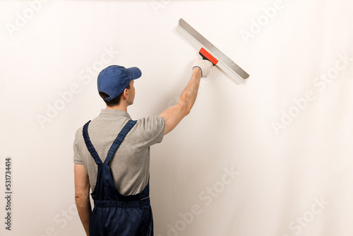 Billede på lærred Worker in wearing overalls and cap plastering a wall with putty using a putty knife