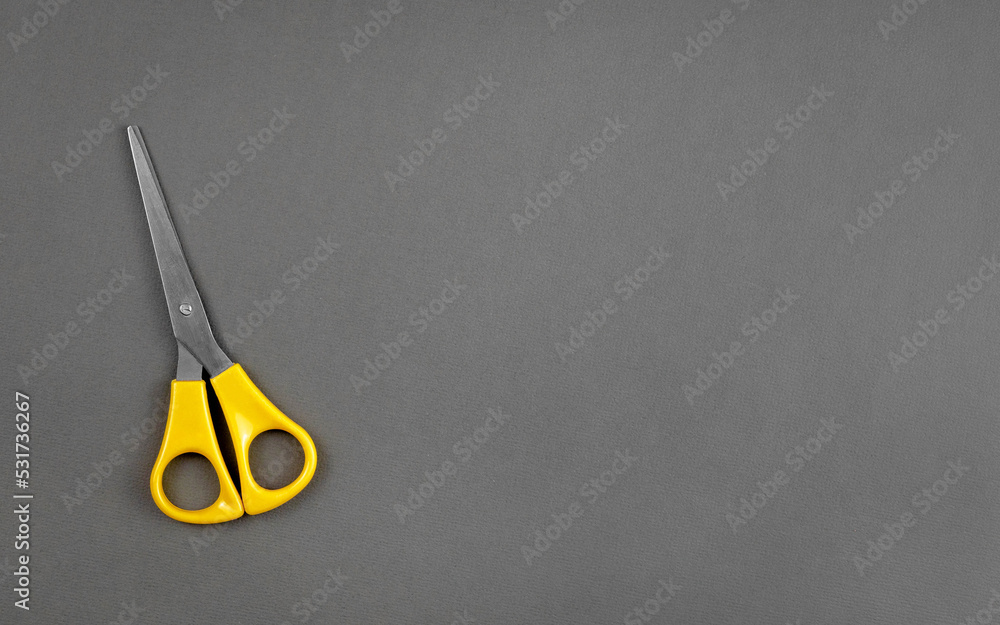 Yellow scissors lie on a gray background with the texture of thick paper Yellow scissors lie on a gray background with the texture of thick paper