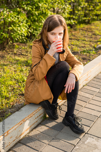 A teenage girl on the street sits on the edge of the road a glass of coffee in her hand. High quality photo